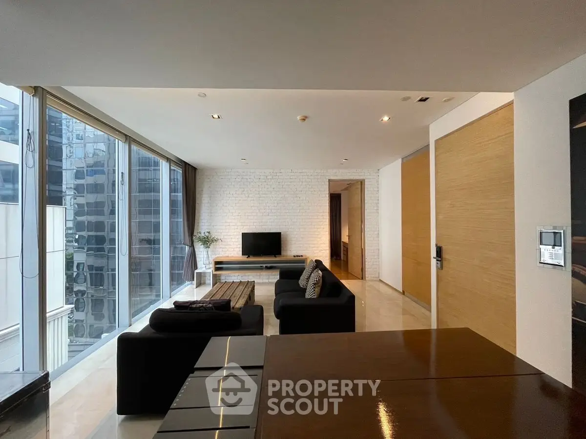 Modern living room with large windows and sleek black furniture in a high-rise apartment.