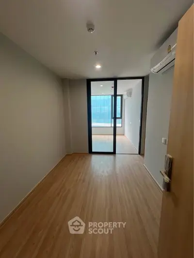 Spacious empty room with wooden flooring and large glass doors leading to a bright balcony.