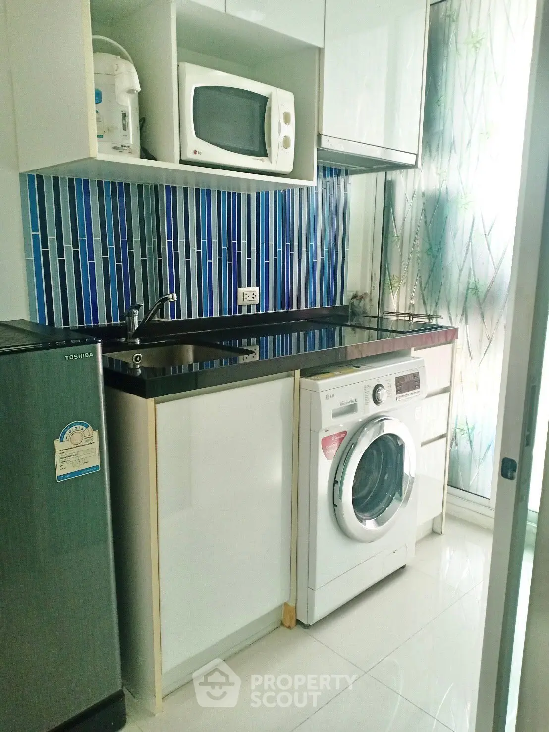 Modern kitchen with washing machine, microwave, and stylish blue backsplash