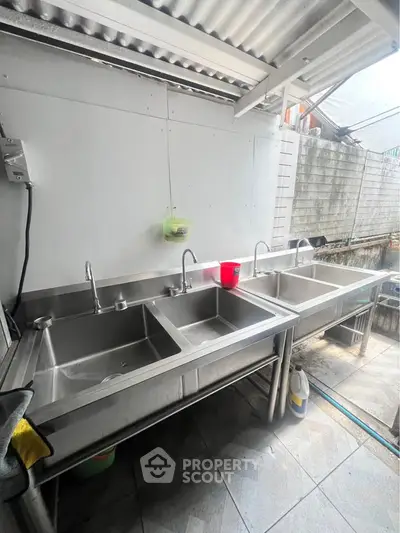 Spacious outdoor kitchen area with stainless steel sinks and tiled flooring, perfect for culinary enthusiasts.