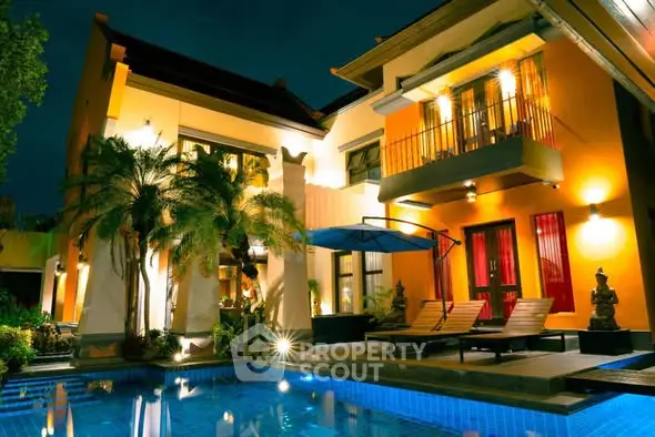 Luxurious villa with illuminated pool and tropical landscaping at night.