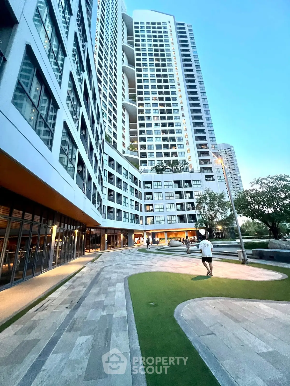 Modern high-rise residential building with landscaped outdoor area and evening lighting.
