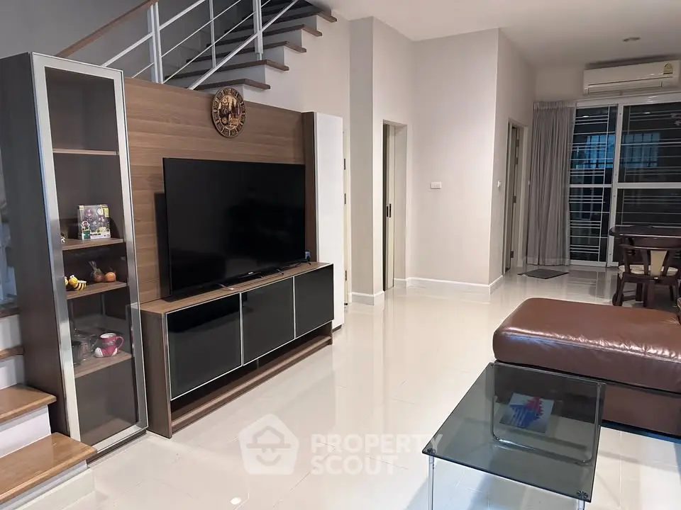 Modern living room with sleek furniture and open layout, featuring a stylish staircase and large TV unit.