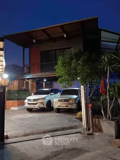 Modern two-story house with spacious driveway and parked cars, showcasing contemporary architecture and outdoor lighting.