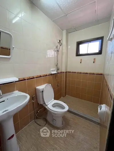 Compact bathroom with shower, toilet, and sink in a tiled interior.