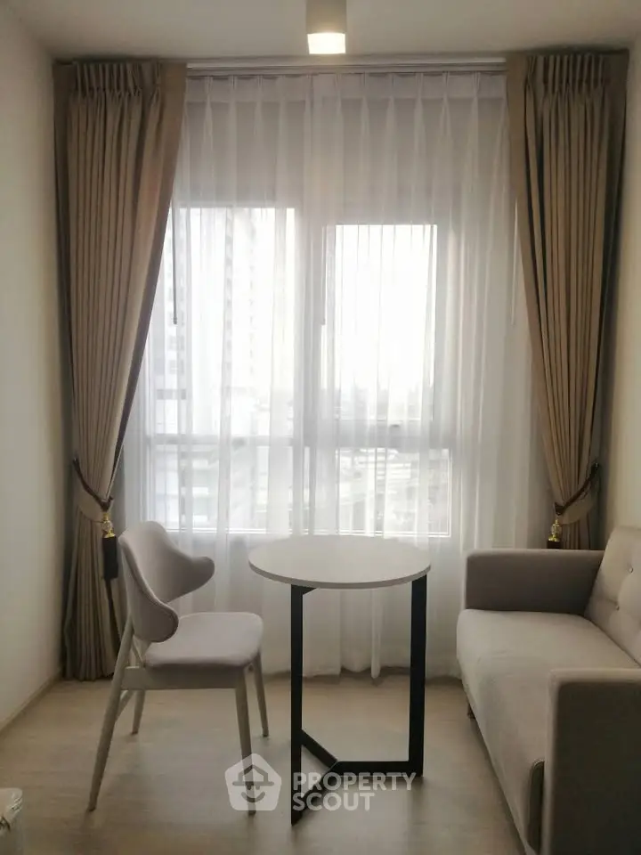 Modern living room with elegant curtains, cozy sofa, and stylish chair around a small table, perfect for urban living.