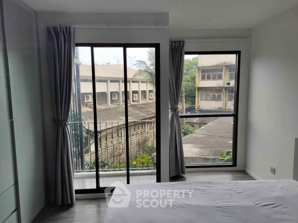 Bright bedroom with large windows and urban view, featuring modern curtains and sleek flooring.