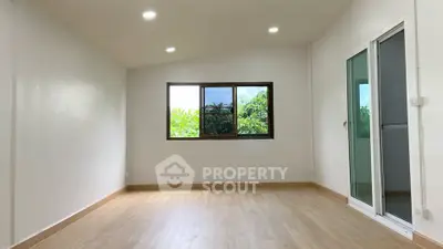 Spacious empty room with wooden flooring and large window offering lush green views.