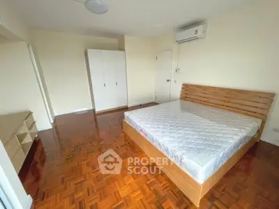 Spacious bedroom with wooden flooring and modern furniture in a bright apartment.