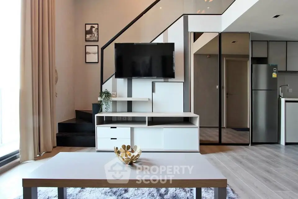Modern living room with stylish decor and open kitchen layout, featuring sleek staircase and wall-mounted TV.