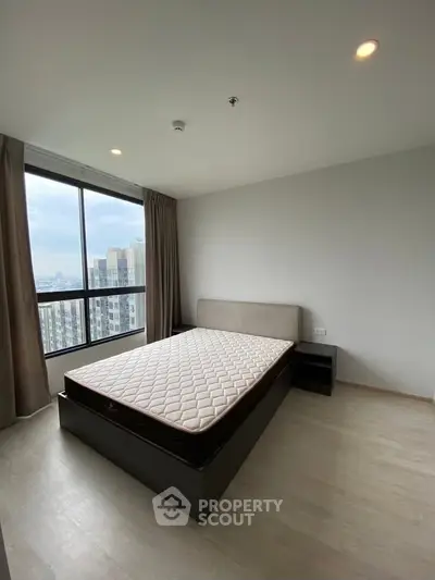 Spacious bedroom with large window offering stunning city views in modern apartment.