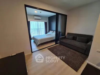 Modern apartment with cozy living room and bedroom separated by glass partition, featuring sleek furniture and natural light.