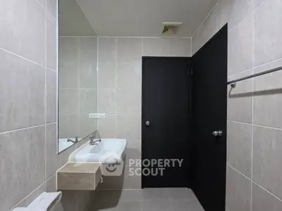 Modern bathroom with sleek design and neutral tiles, featuring a wall-mounted sink and large mirror.
