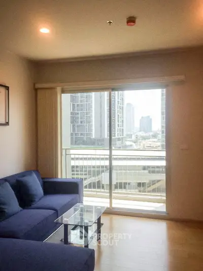Modern living room with blue sofa and city view from balcony in high-rise apartment.