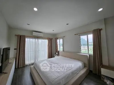Spacious bedroom with large windows and modern decor, offering serene views and ample natural light.