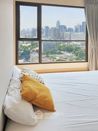 Bright bedroom with city view from large window, featuring cozy pillows and modern decor.