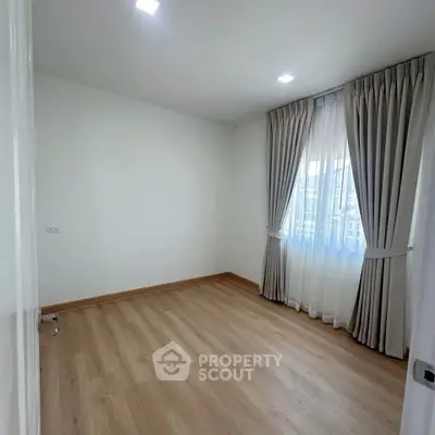 Spacious empty room with wooden flooring and large window with curtains, perfect for customization.