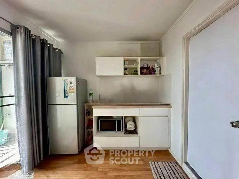 Modern kitchen with fridge, microwave, and open shelving in a bright apartment.