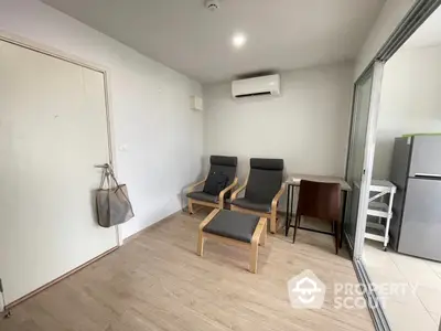 Spacious and modern living room with sleek wooden flooring, comfortable seating, and ample natural light streaming in from the large glass door leading to a balcony.