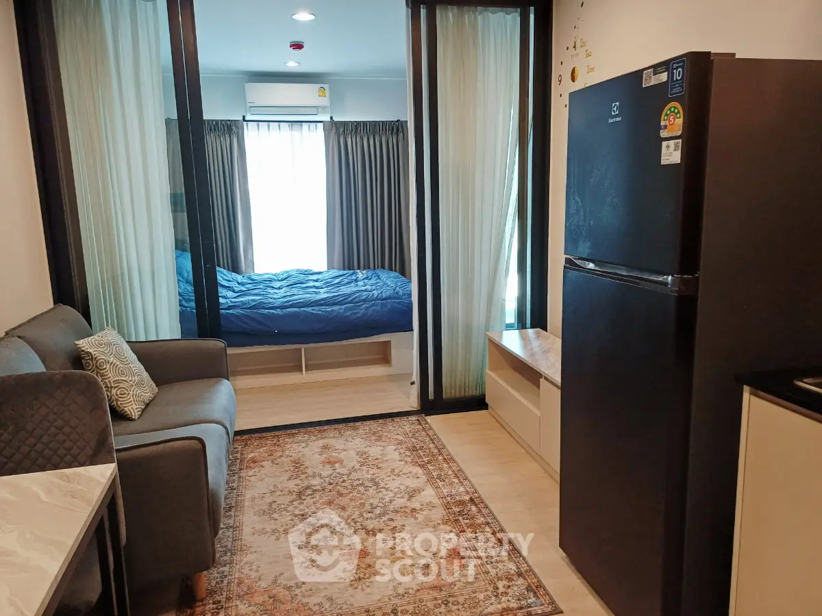 Modern studio apartment with cozy living area and bedroom, featuring a sleek refrigerator and elegant decor.