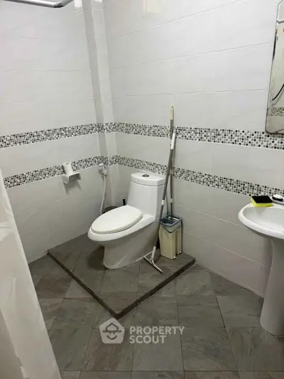 Modern bathroom with tiled walls and floor, featuring a toilet and sink.