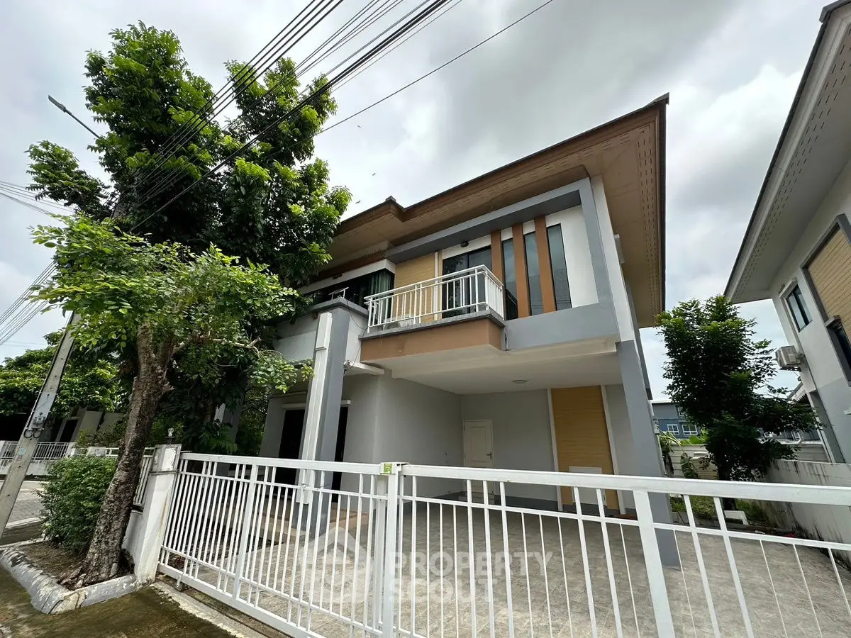 Modern two-story house with balcony and gated driveway in suburban neighborhood.