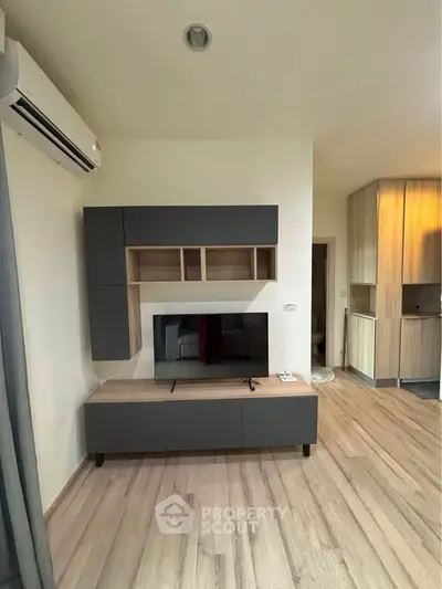 Modern living room with sleek cabinetry and wooden flooring, featuring a mounted TV and air conditioning unit.