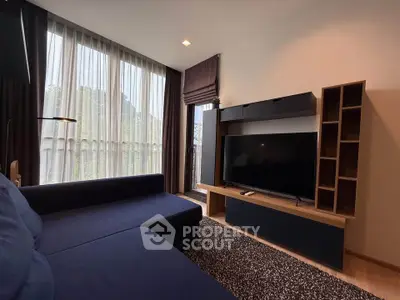 Modern living room with large TV and stylish furniture, featuring floor-to-ceiling windows.