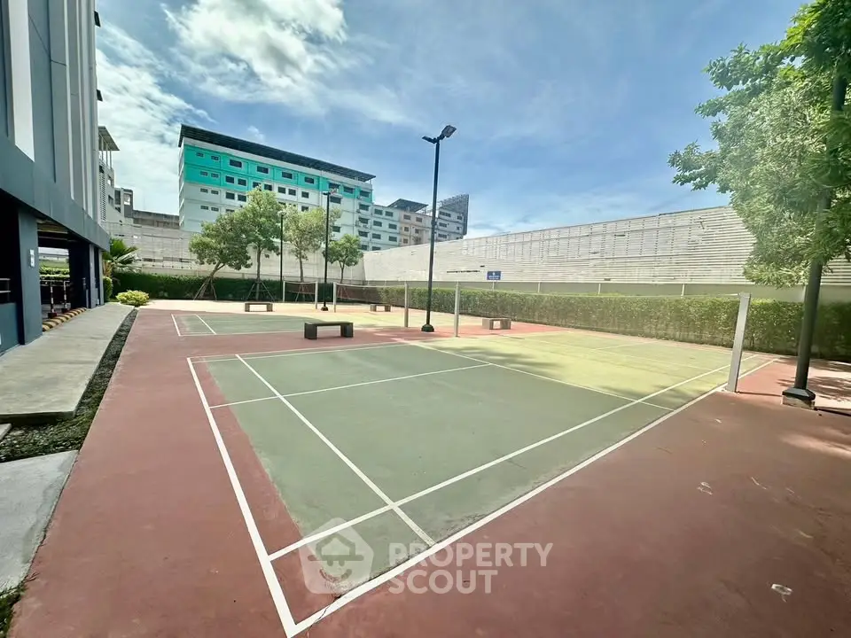 Spacious outdoor tennis court in modern residential complex with lush greenery and clear blue sky.