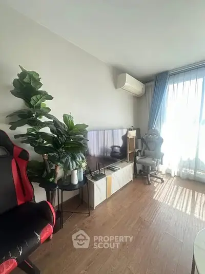 Modern living room with gaming chair, TV, and large window with natural light.