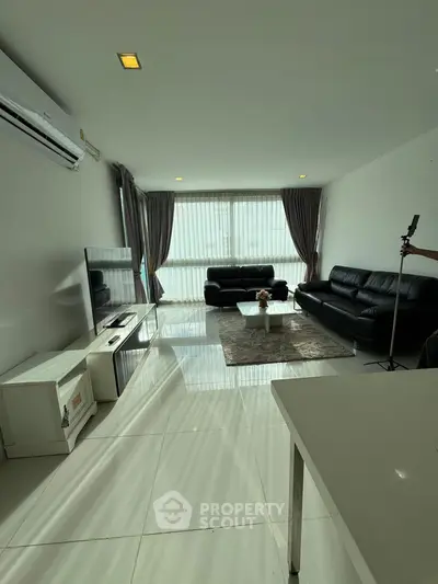 Spacious modern living room with sleek black leather sofas and large windows for natural light.