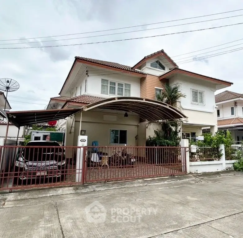 Charming two-story house with carport and lush greenery in a serene neighborhood.