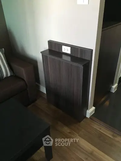 Modern living room corner with sleek wooden panel and power outlet, adjacent to a stylish sofa.