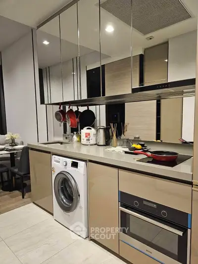 Modern kitchen with sleek cabinetry, built-in oven, and washing machine, featuring a stylish open layout.