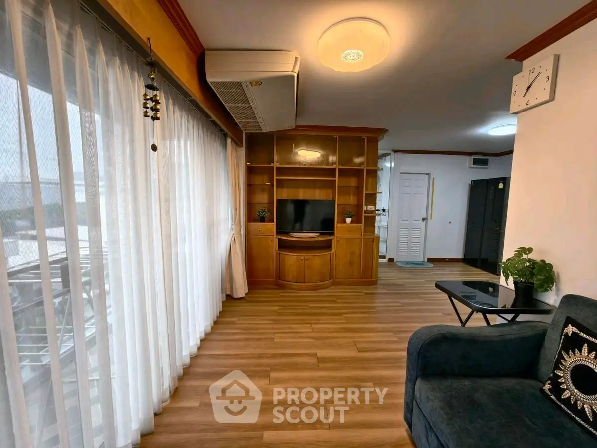 Spacious living room with wooden flooring and modern decor, featuring large windows and stylish furniture.