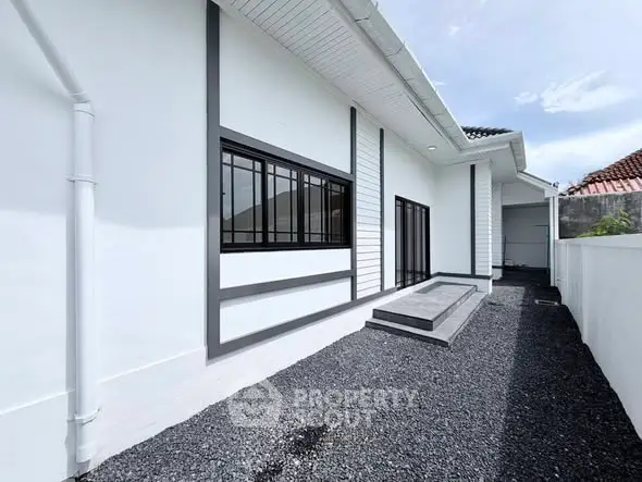 Modern white exterior of a house with sleek black window frames and gravel pathway.