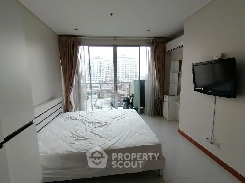 Spacious bedroom with large window and city view, featuring modern furnishings and natural light.