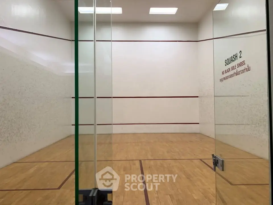 Spacious indoor squash court with wooden flooring and glass walls in a modern sports facility.