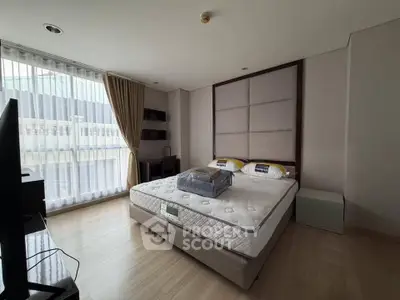 Spacious bedroom with large window and modern furnishings in a luxury apartment.