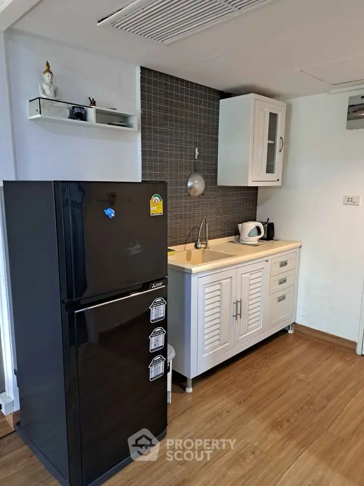 Compact kitchen with black fridge and white cabinets, ideal for modern living.