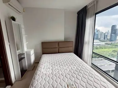 Modern bedroom with city view, large window, and minimalist decor in high-rise apartment.