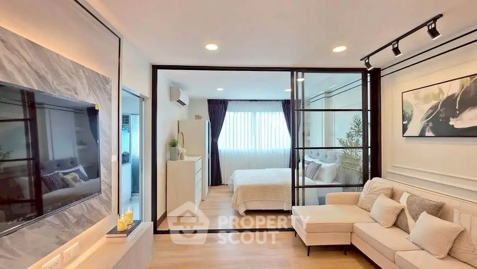 Modern open-plan living room with glass partition and cozy bedroom view.