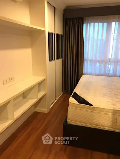 Cozy bedroom with wooden flooring, large window, and built-in storage in modern apartment.