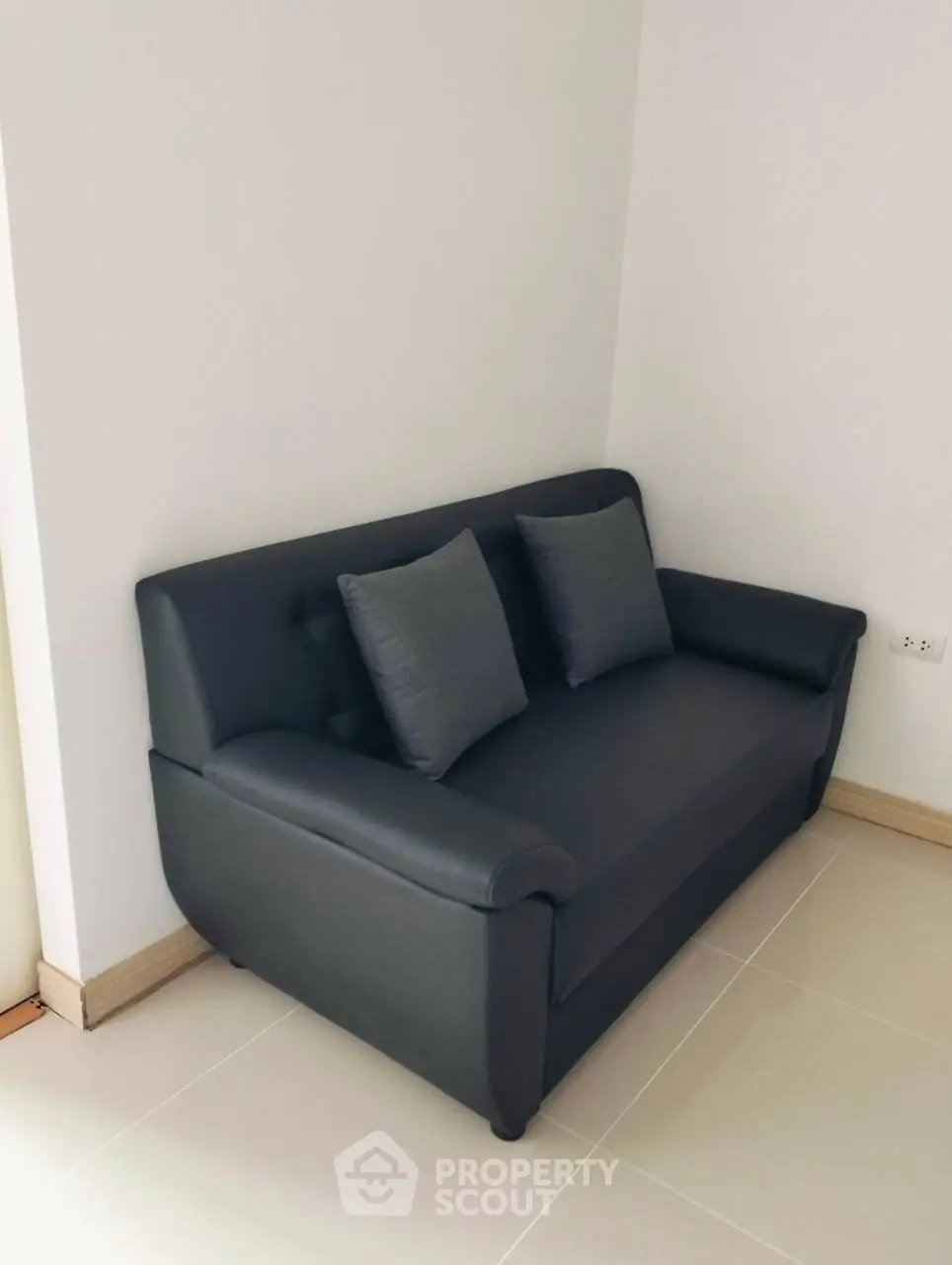 Modern black leather sofa in a minimalist living room corner with tiled flooring.