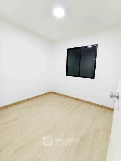 Minimalist empty room with wooden flooring and a window, perfect for customization.