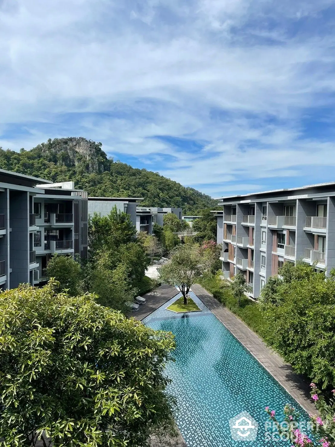 Luxurious resort-style condominium complex with a stunning infinity pool, lush greenery, and a majestic mountain backdrop, offering a serene living experience.