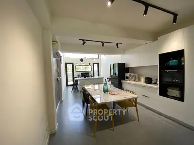 Modern kitchen with sleek white cabinets, dining table, and natural light.