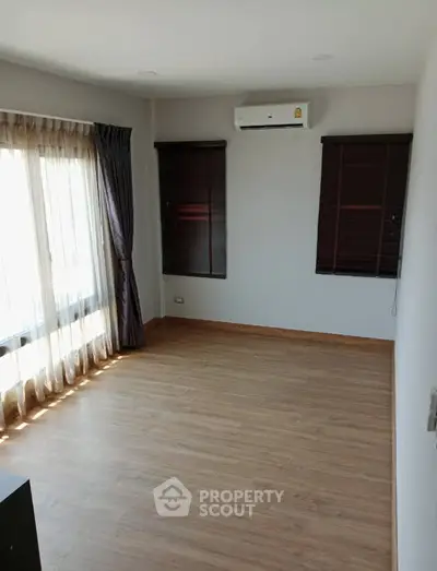 Spacious empty room with wooden flooring and large windows, perfect for customization.