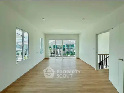 Spacious living room with wooden flooring and large windows offering natural light and balcony access.