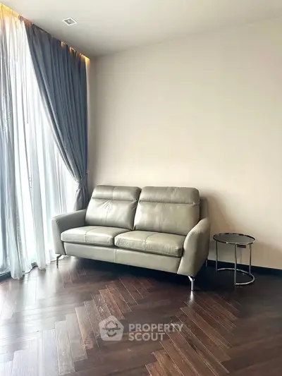Modern living room with sleek leather sofa and elegant curtains, featuring dark wood flooring.